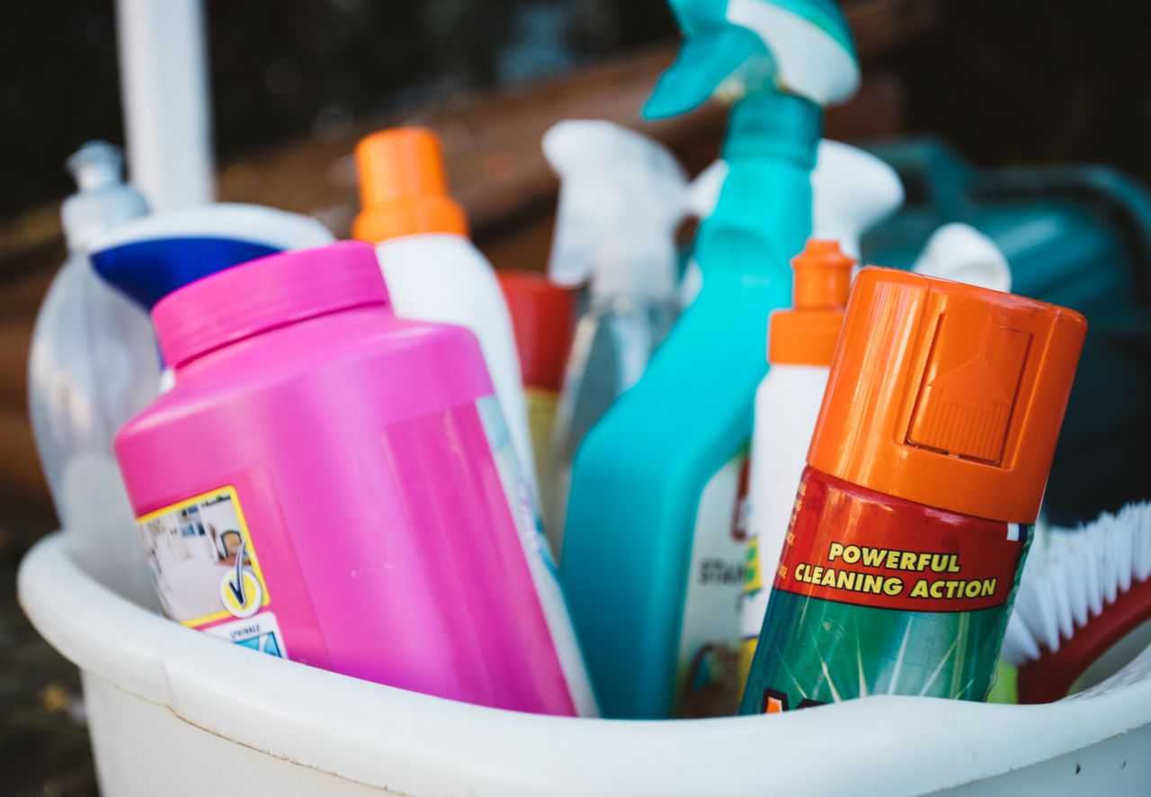 services-03 Close-up of assorted cleaning supplies in a bucket outdoors, showcasing various detergents and sprays.
